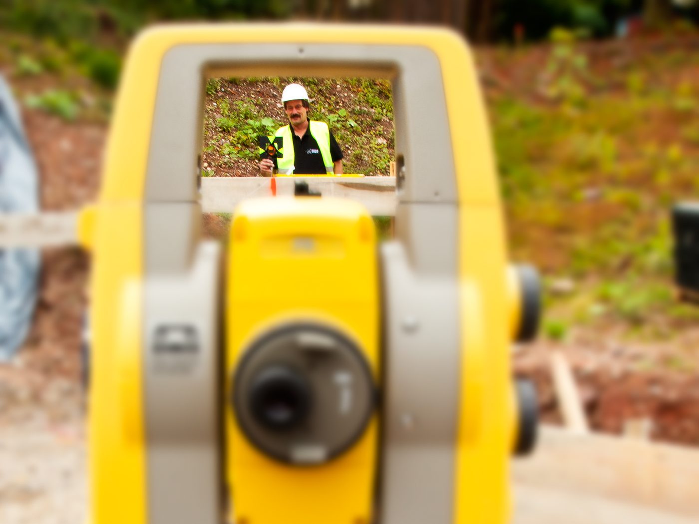 Blick durch den Sucher eines Tachymeters auf einen Vermessungstechniker mit Reflektorstab